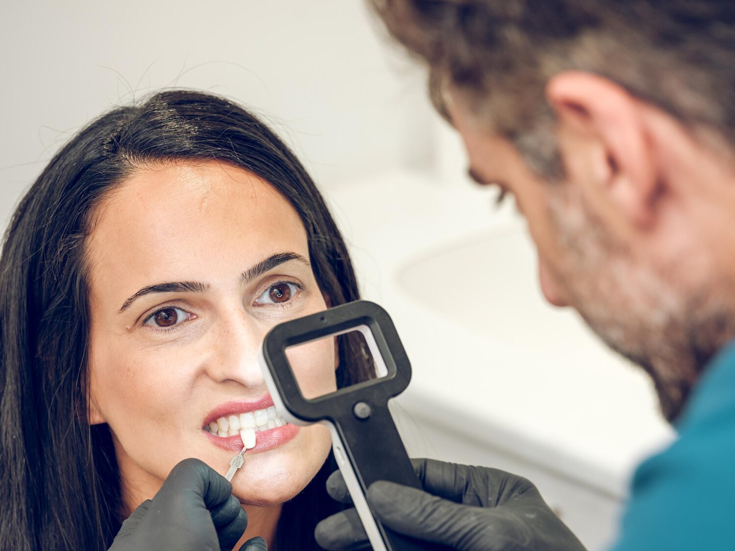 Focused dentist latex gloves with loupe comparing teeth color woman implant while working modern clinic 935394 2407 Focused dentist latex gloves with loupe comparing teeth color woman implant while working modern clinic 935394 2407